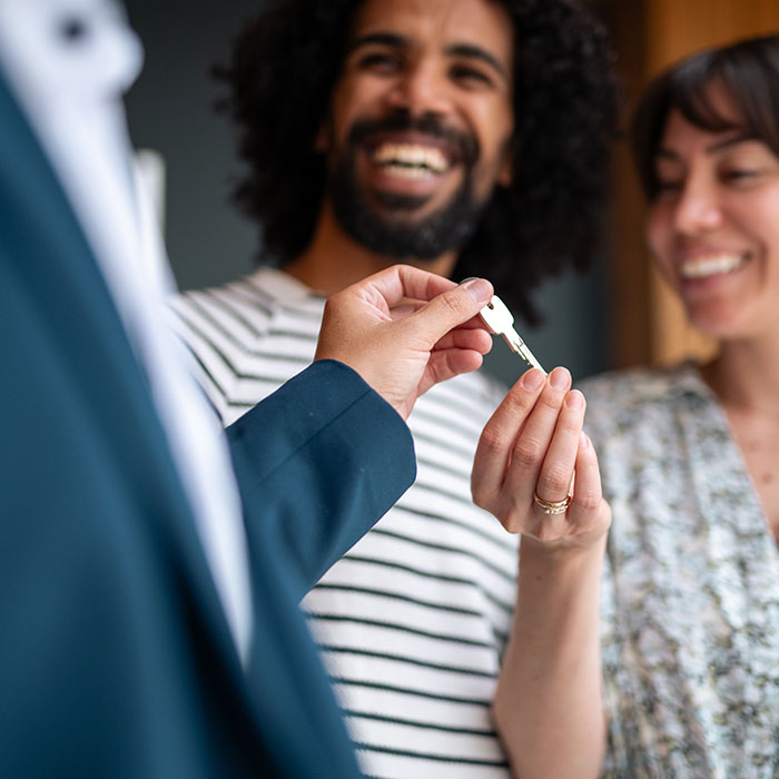 A professional real estate agent hands over keys to a smiling diverse couple