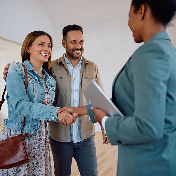Happy woman shaking hands with real estate agent while buying new apartment with her husband